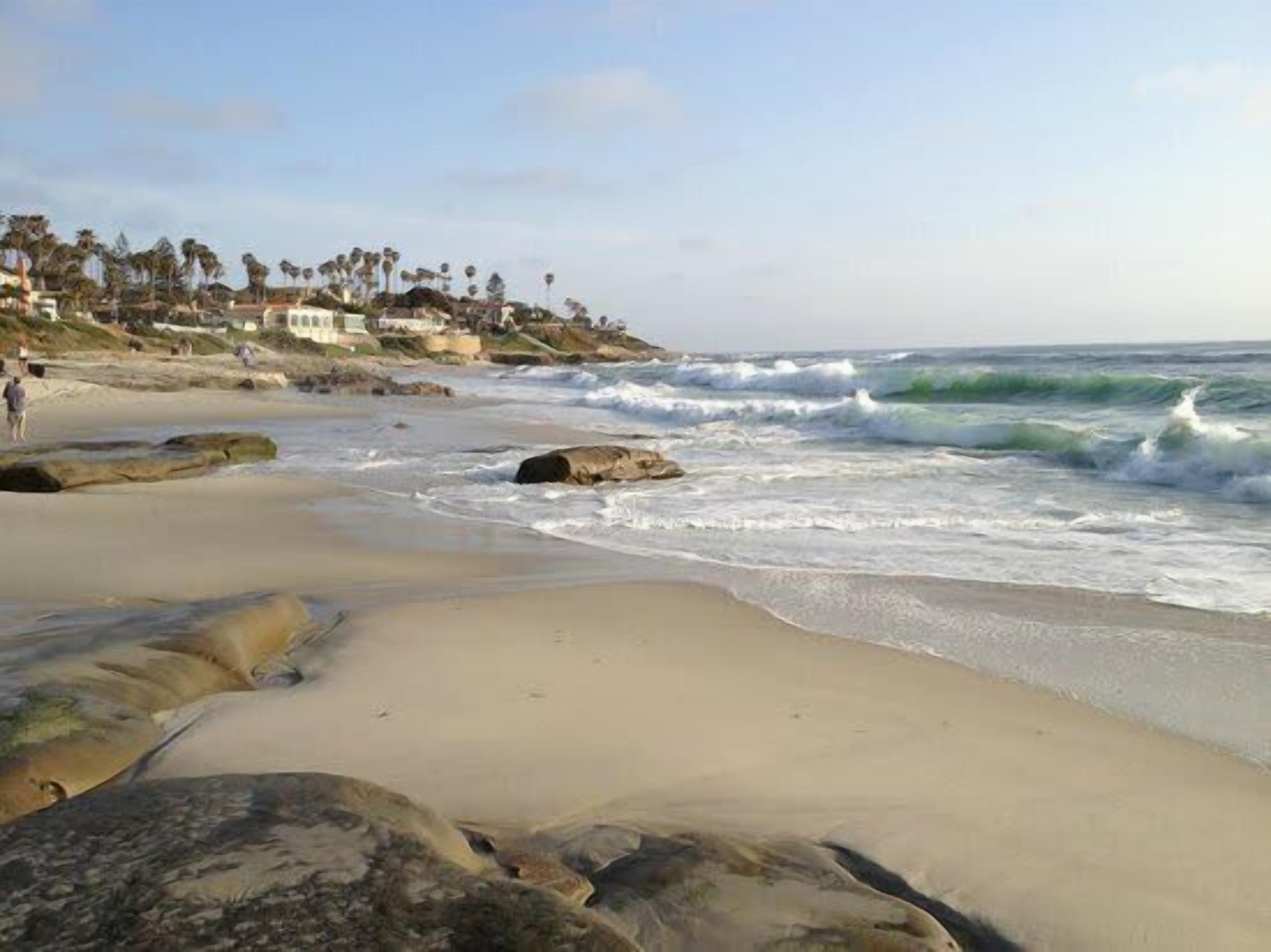 A beach with waves, rocks, and a few people.
