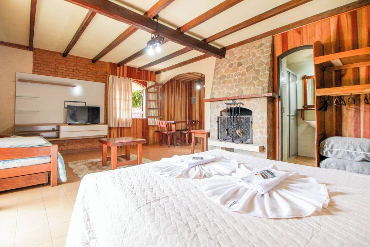 Quarto com cama, televisão, lareira e parede de pedra.