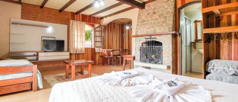 A bedroom with a bed, a TV, a fireplace, and a stone wall.