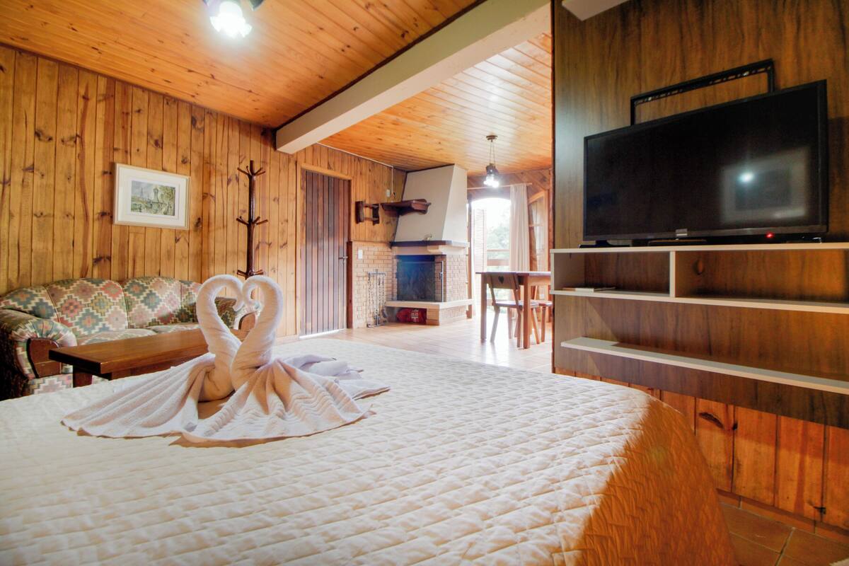 Um quarto aconchegante com uma cama, televisão, lareira e paredes de madeira.