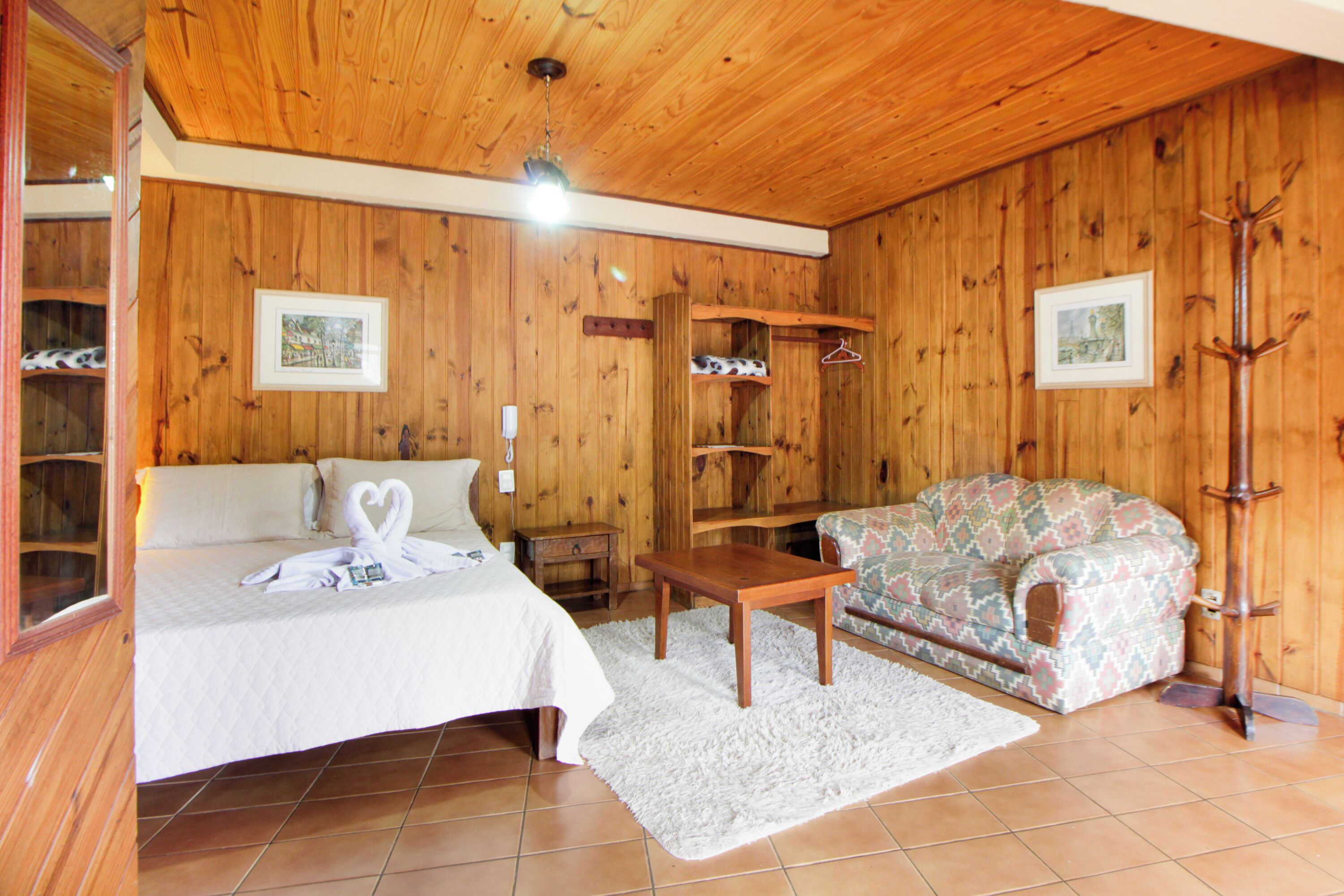 A wooden-paneled room with a bed, a sofa, a coat rack, and a small table.