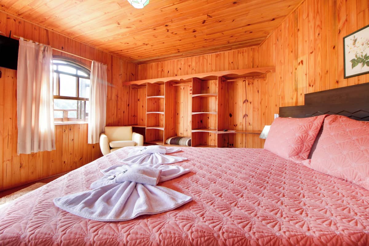 Quarto de cabana de madeira com cama, cadeira e estantes embutidas.