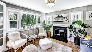 A cozy living room with a fireplace, large windows, and comfortable seating. - Stylish Cape Escape on Bank St RPAM070 (Harwich)