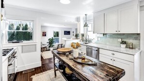 A modern kitchen with white cabinetry, a wooden island, and a large window. - Stylish Cape Escape on Bank St RPAM070 (Harwich)