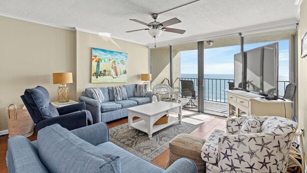 A spacious living room with a ceiling fan, a sofa set, a coffee table, and a TV. - ~ Oceanfront Oasis ~  Private Condo ~ 3 Bedroom (Myrtle Beach)