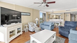 A living room with a flat-screen TV, white entertainment unit, blue sofas, and a ceiling fan. - ~ Oceanfront Oasis ~  Private Condo ~ 3 Bedroom (Myrtle Beach)