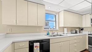 A modern kitchen with beige cabinets, a dishwasher, a sink, and a window providing a view of the city. - ~ Oceanfront Oasis ~  Private Condo ~ 3 Bedroom (Myrtle Beach)