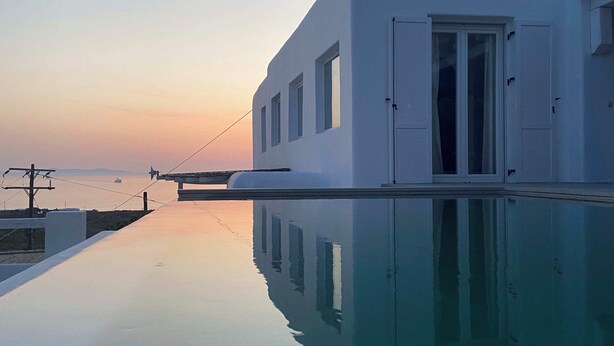 Un edificio moderno blanco con un estanque reflectante al frente, una puerta y ventanas.