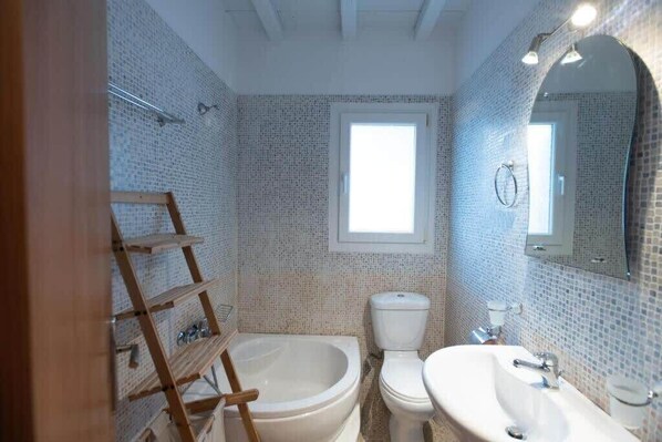 Ein Badezimmer mit Badewanne, Toilette und Waschbecken, mit Fliesenwänden und einem Fenster.