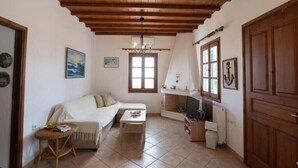 A cozy living room with a wooden ceiling, a sofa, a small table, a television, and a window with curtains. - Mykonos Elegance 2-Bedroom Escape in Psarou (Platis Gialos Mykonos)