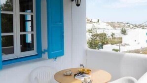 A balcony with a white wall, blue shutters, a small round table with chairs, and a view of buildings in the distance. - Mykonos Elegance 2-Bedroom Escape in Psarou (Platis Gialos Mykonos)