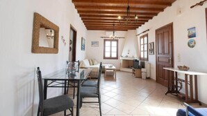 A spacious living area with a wooden ceiling, a dining table with chairs, a sofa, and a television in the background. - Mykonos Elegance 2-Bedroom Escape in Psarou (Platis Gialos Mykonos)