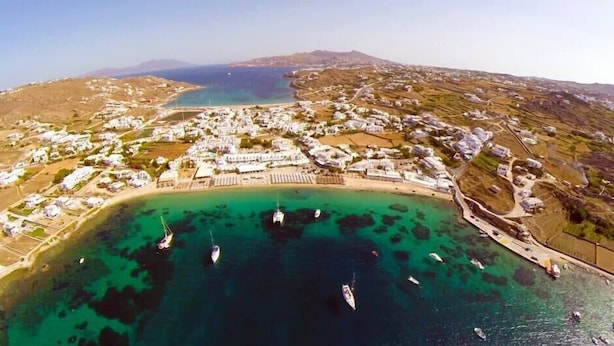 Una vista aerea di una cittadina costiera con edifici bianchi, una spiaggia e imbarcazioni in acqua.