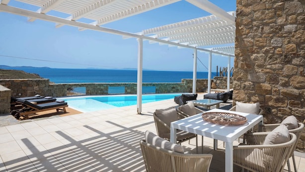 Un espace aménagé au bord de la piscine, avec vue sur la mer, agrémenté d’une pergola, de murs en pierre et de mobilier d’extérieur.