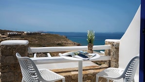 Un balcon avec des chaises et une table en métal blanc, donnant sur un paysage côtier avec des bâtiments et la mer.