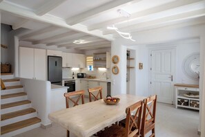 Une cuisine moderne avec des meubles blancs, un coin repas doté d’une table et de chaises en bois, et un escalier avec des marches en bois.