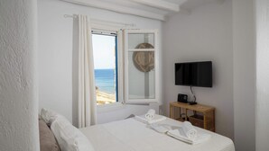 Une chambre à coucher avec un lit, une télévision, une fenêtre avec des rideaux et une vue sur la plage.