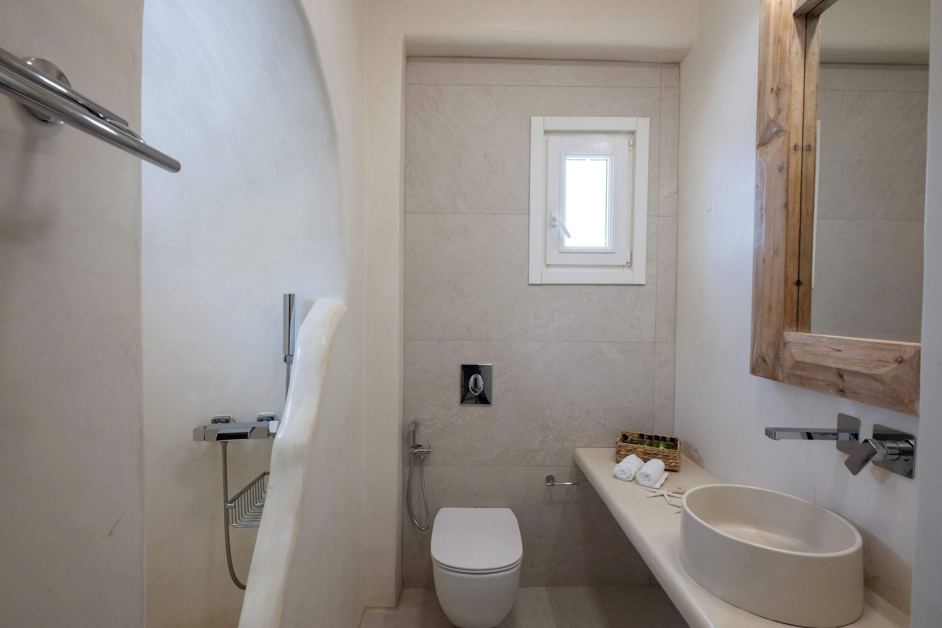 A bathroom with a toilet, a shower, a sink, and a small window.