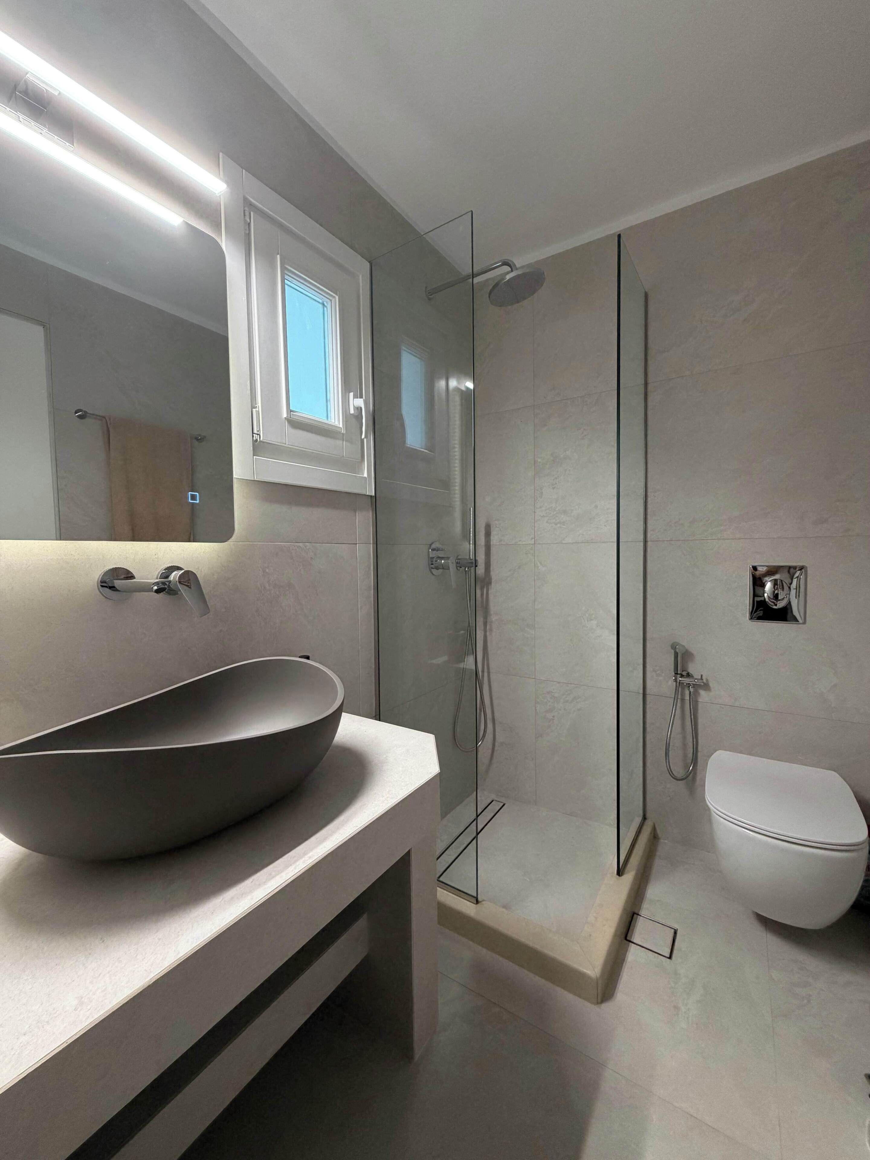 A modern bathroom with a large vessel sink, a glass-enclosed shower, and a toilet.