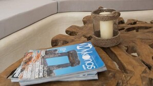 Una sala de estar con un sofá gris, una mesa de centro de madera con una vela y revistas, y un cuadro con motivos playeros en la pared.