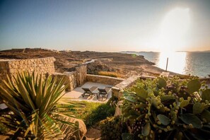 A coastal property with a stone wall, outdoor seating, and cacti. - Romantic Mykonian Oasis Suite w Jacuzzi & Sea View (Mykonos)