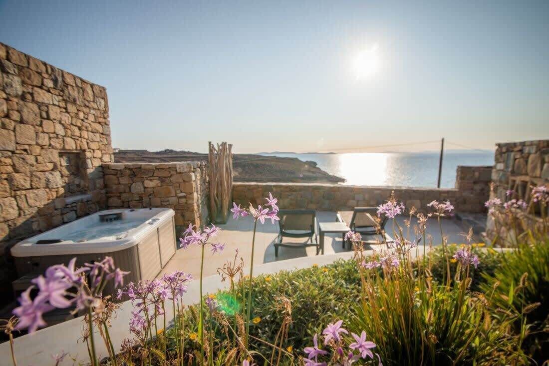 A stone-walled outdoor area with a hot tub, seating, and a view of the sea.