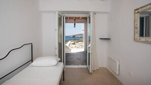 A bedroom with a bed, a view of the outdoors through an open door, a radiator, and a mirror on the wall. - Amazing Views At Agios Sostis Beach In Mykonos (Mykonos)