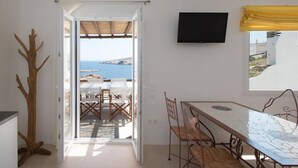A room with a view of the sea, a dining table, chairs, a TV, and a wooden decor piece. - Amazing Views At Agios Sostis Beach In Mykonos (Mykonos)