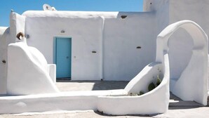 A white-walled building with a blue door, a small window, and a satellite dish. - Amazing Views At Agios Sostis Beach In Mykonos (Mykonos)