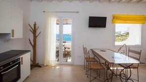 A modern kitchen with a dining area, a TV mounted on the wall, and a view of the sea through the window. - Amazing Views At Agios Sostis Beach In Mykonos (Mykonos)