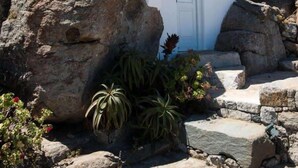 A white building with a door, surrounded by large rocks and some plants.