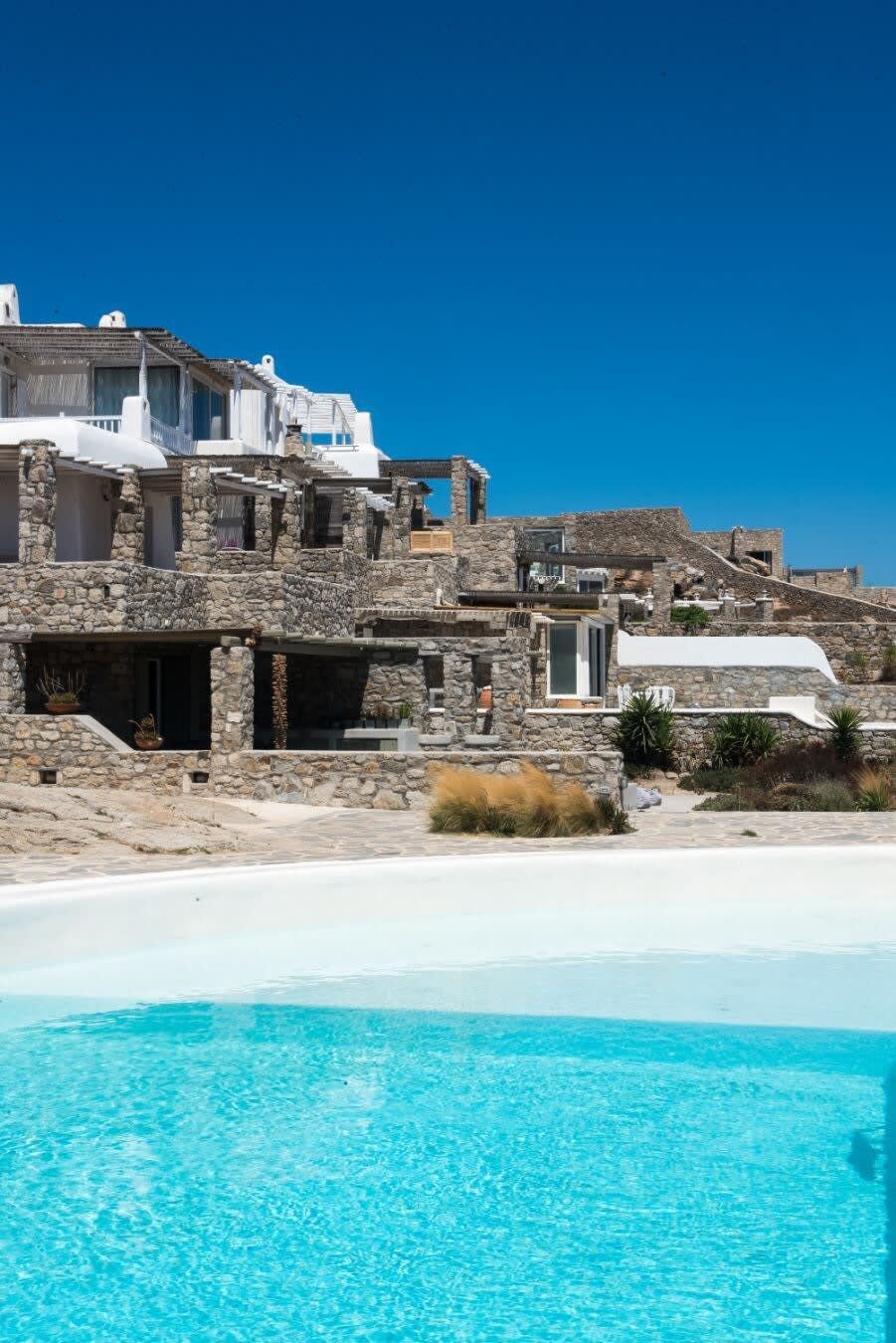 Un bâtiment situé sur la côte, doté d’une piscine, de murs en pierre et surplombant un ciel d’un bleu limpide.