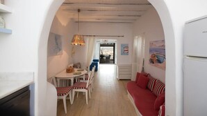A narrow hallway with a dining area on one side and a living area on the other, featuring a red sofa and a white table with chairs.