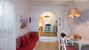 A cozy living room with a red sofa, a dining table set for two, and an archway leading to a kitchen.