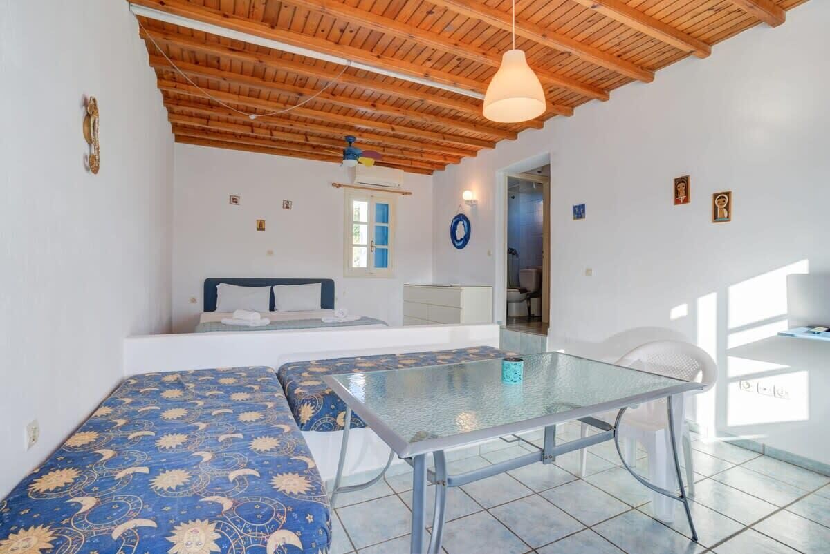 A room with a bed, a glass table, and a ceiling with wooden beams.