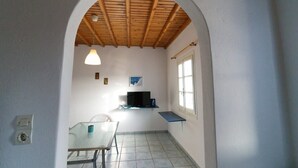 Ein kleiner Raum mit Fliesenboden, einem Tisch mit Stühlen, einem Fernseher auf einem Regal und einem Fenster mit Blick.