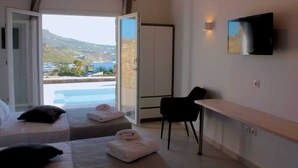 A hotel room with two beds, a desk, a chair, a TV, and a view of a pool and landscape. - Mykonian Luxury Light Blue Villa with Private Pool (Mykonos)