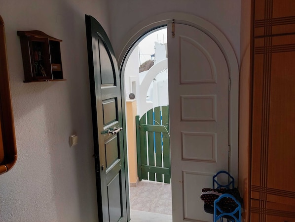 A hallway with a white door leading to an outdoor area with a green gate.