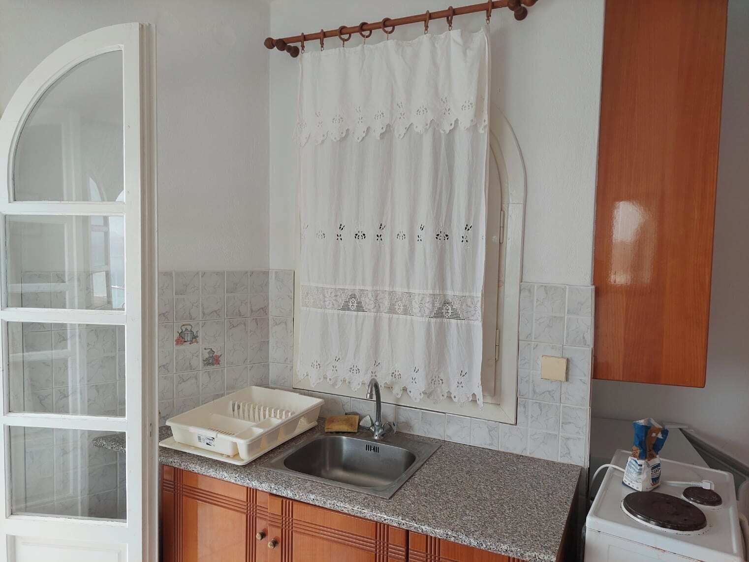 A kitchen with a sink, a white cabinet, and a window with a curtain.