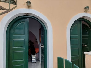 A doorway with a metal heater inside, leading to a room with a bed and a person sitting.