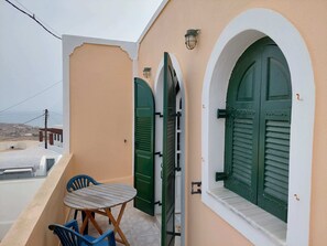 A balcony with a table and chairs, green shutters, and a view of the landscape.