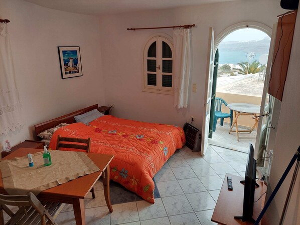A bedroom with a bed, a table with chairs, a TV, and a balcony with a view of the sea.