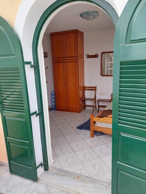 Een kamer met een houten garderobe, een stoel, een bed en een betegelde vloer.