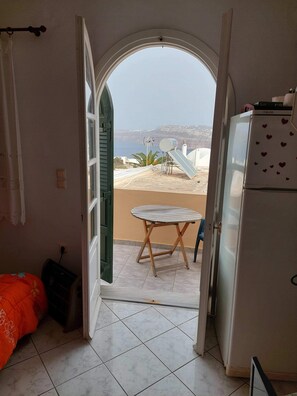 A room with a view of the sea, a small table, and a refrigerator.