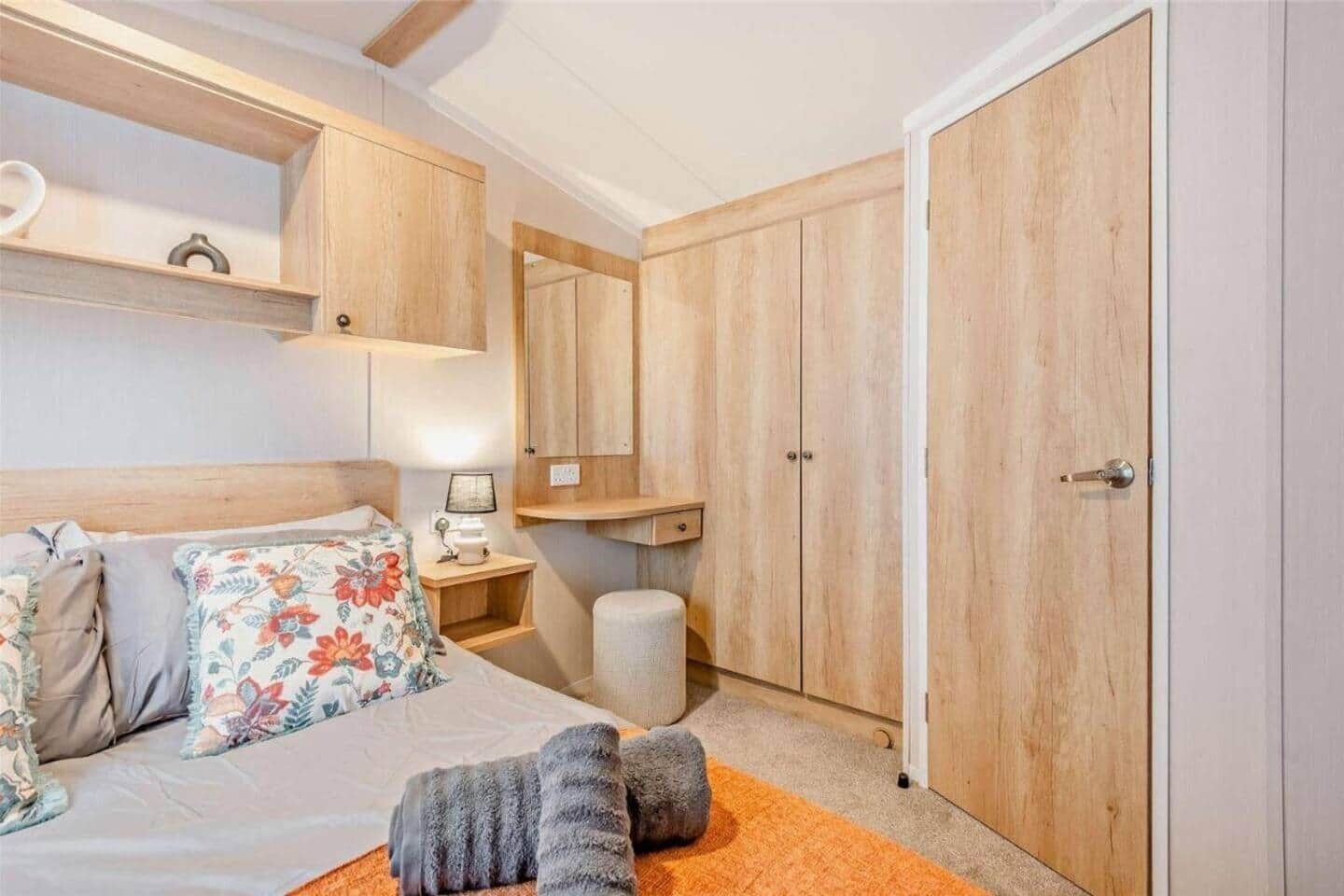 Un dormitorio con cama, mesita de noche, lámpara, armario y un taburete pequeño.