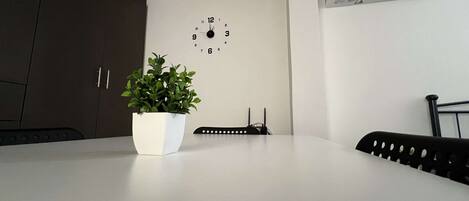 A modern kitchen with a white countertop, a potted plant, a clock, and an air conditioning unit on the wall.