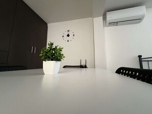 A modern kitchen with a white countertop, a potted plant, a clock, and an air conditioning unit on the wall. - Charming Getaway in the Heart of Emporio Santorini (Santorini)