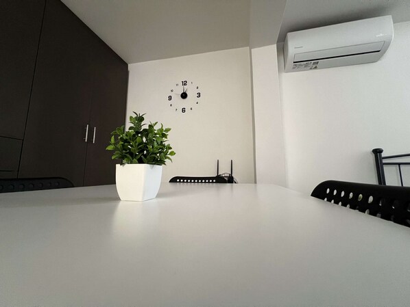 Une cuisine moderne avec un plan de travail blanc, une plante en pot, une horloge et un appareil de climatisation fixé au mur.