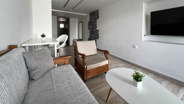 Un salon moderne comprenant un canapé, un fauteuil, une table basse et un téléviseur fixé au mur.