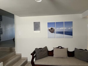 A modern living room with a sofa, a staircase, and a wall-mounted artwork. - Charming Getaway in the Heart of Emporio Santorini (Santorini)